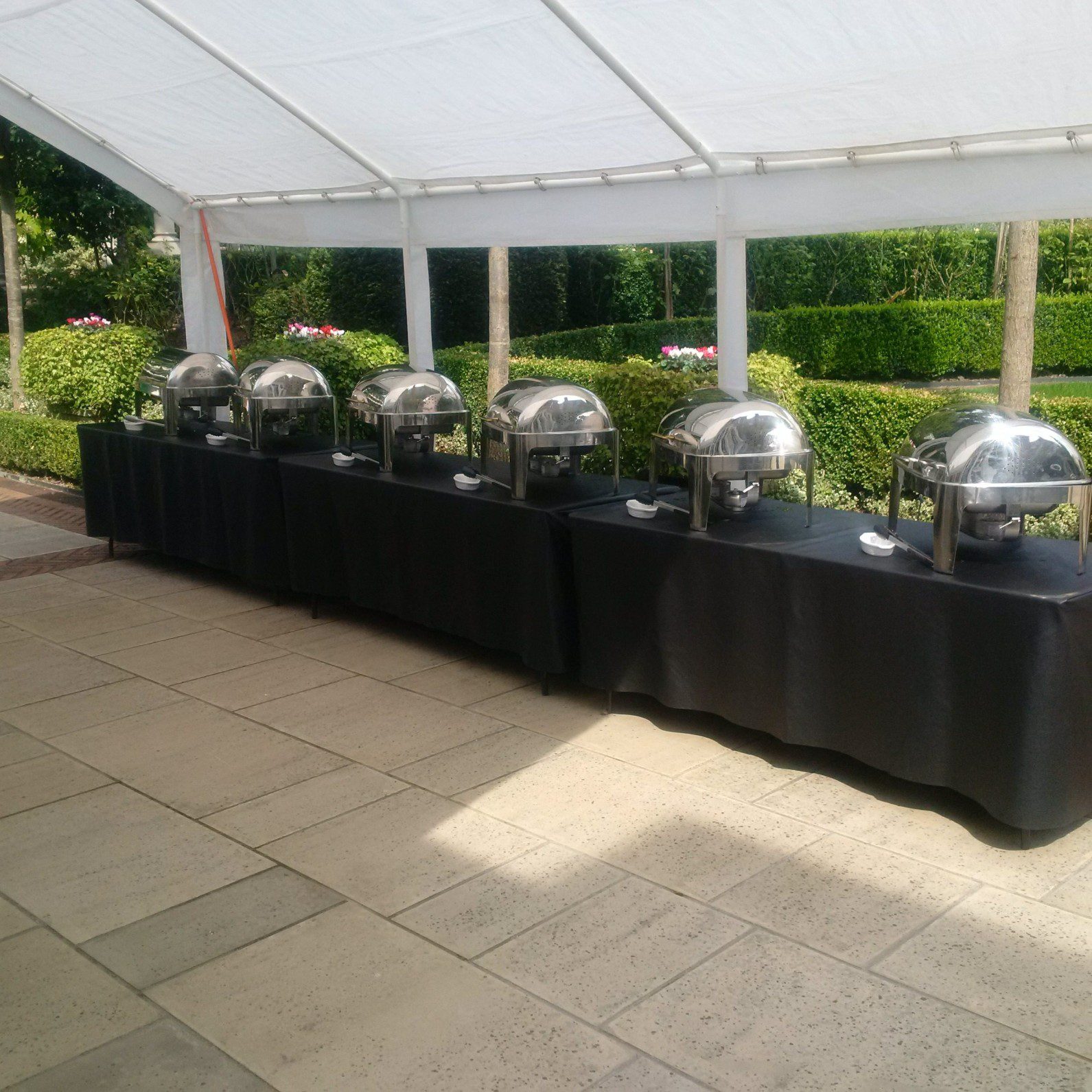Chafing dishes on black trestle table inside open marquee
