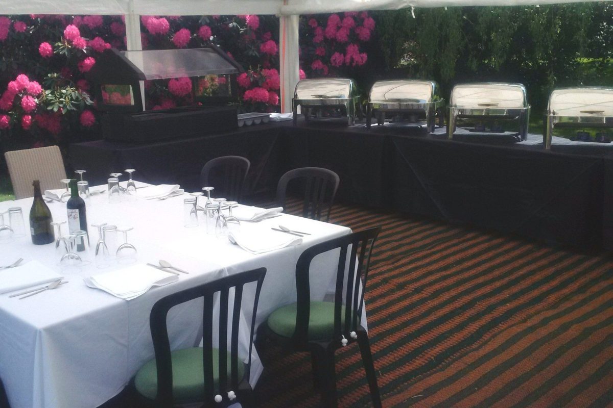 Covered table with wine bottles in the centre and chairs under marquee